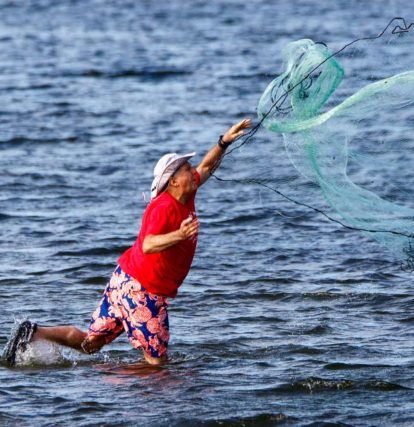 man throwing a large net into the water
